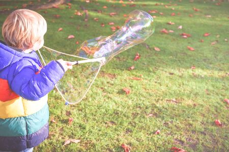 Child playing outside in a garden during day time with bubbles he is happy and runningの写真素材