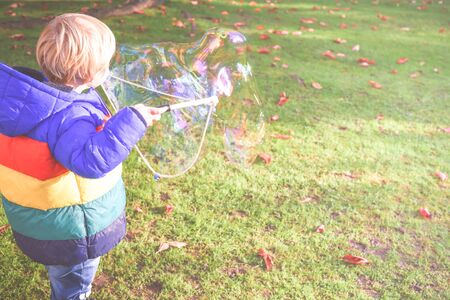 Child playing outside in a garden during day time with bubbles he is happy and runningの写真素材