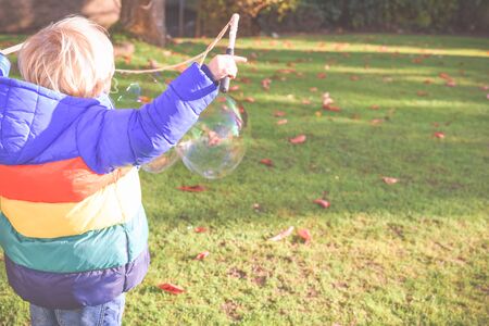 Child playing outside in a garden during day time with bubbles he is happy and runningの写真素材