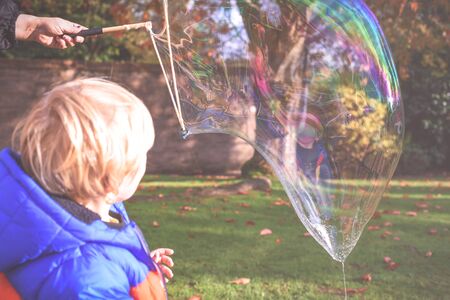 Child playing outside in a garden during day time with bubbles he is happy and running