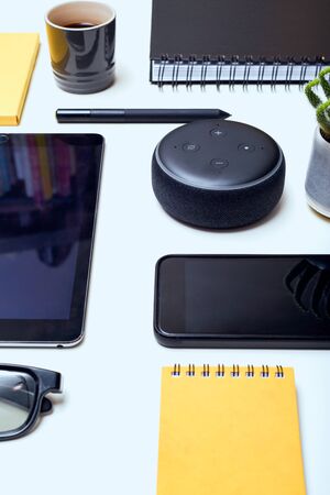 Digital and wireless technology objects arranged on a white desk including phone tablet and smart home speakerの写真素材
