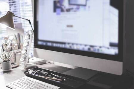Blurred large computer screen on a home office desk interior eith work objects in backgroundの写真素材