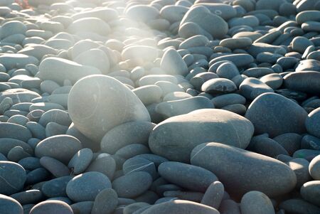 A beam of sunlight shines onto a rock in a collection of pebbles