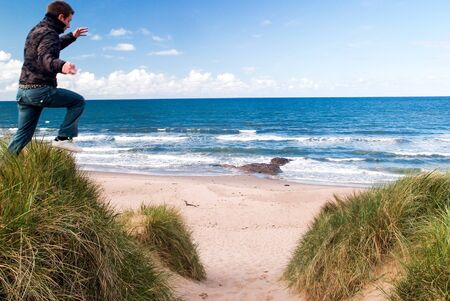 Man jumping from a high sand dune to the sand on the beach on a sunny winter dayの写真素材
