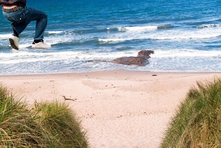 Man jumping from a high sand dune to the sand on the beach on a sunny winter dayの写真素材