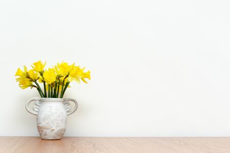 Flowers in a rustic style vase on wooden table with white interior wall background, daffodilsの写真素材