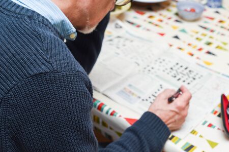 Mature man doing a crossword puzzle and relaxing at home during the day, indoor shotの写真素材