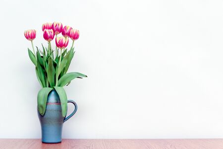 Pink tulips flowers in a vase on wooden table with white interior wall backgroundの写真素材
