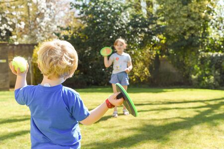 Children playing outside a brother and sister play a ball game in a garden