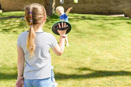 Children playing outside a brother and sister play a ball game in a gardenの写真素材
