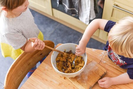 Children stir a mixing bowl in the kitchen at home while baking cookiesの写真素材
