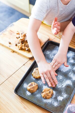 Kids making cookies in kitchen placing dough on tray for cooking at homeの写真素材