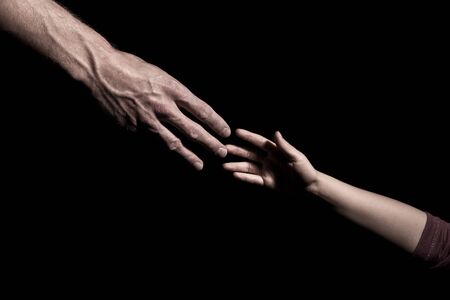 Hands reaching out to each other on dark black backgroundの写真素材