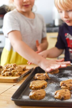 Kids making cookies in kitchen placing dough on tray for cooking at homeの写真素材