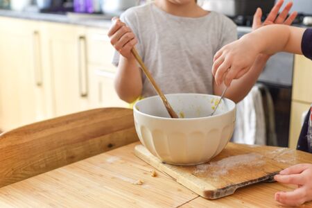 Children stir a mixing bowl in the kitchen at home while baking cookiesの写真素材