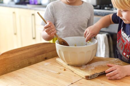 Children stir a mixing bowl in the kitchen at home while baking cookiesの写真素材