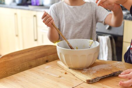 Children stir a mixing bowl in the kitchen at home while baking cookiesの写真素材