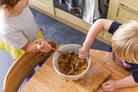Children stir a mixing bowl in the kitchen at home while baking cookiesの写真素材