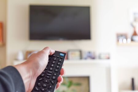 Hand with tv remote control switching television on at home