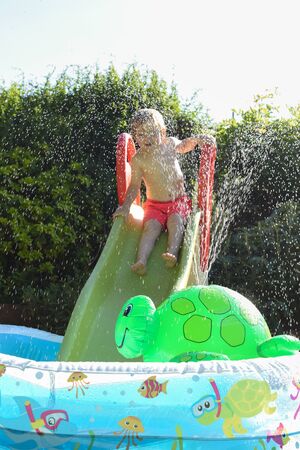 Child having fun playing in water in a garden paddling pool the boy is happy and smilingの写真素材