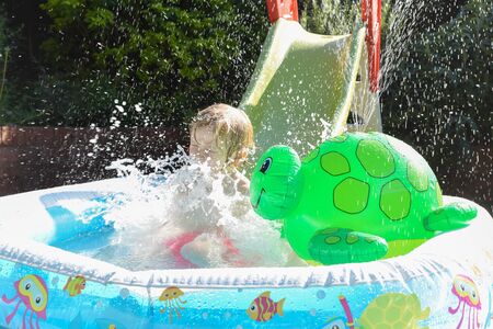 Child having fun playing in water in a garden paddling pool the boy is happy and smiling