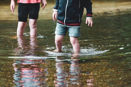 Children paddle in a stream of water outside during a sunny day out togetherの写真素材