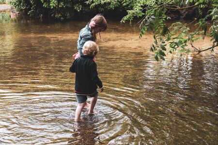 Children playing outside in a shallow stream paddling in the waterの写真素材