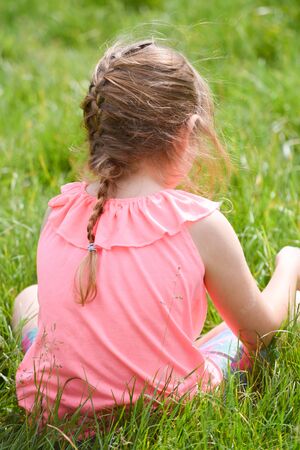 Child sitting in a field of grass outside on summer dayの写真素材