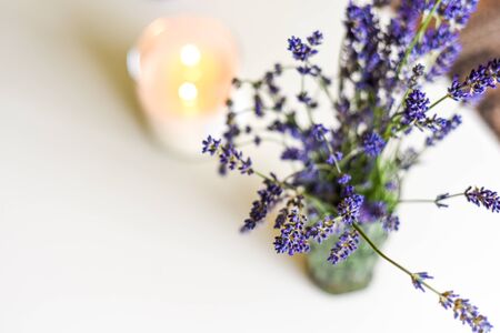 Scented candle and lavender flowers on white coffee table in home interior
