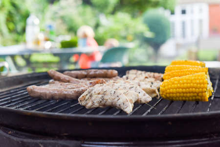 Family bbq outside in a garden with food on the barbecue grill cooking outdoors and people in the backgroundの写真素材