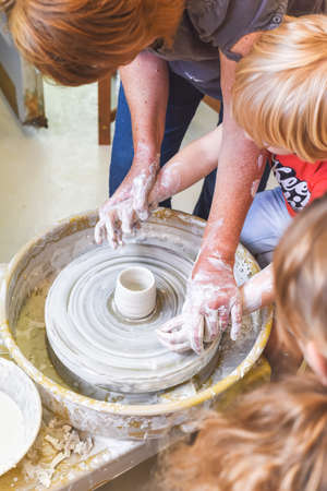 Children learning to make pottery as a hobby with their grandmother in a ceramics workshopの写真素材