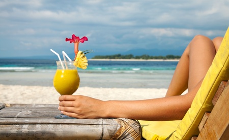 Woman holding a fruit cocktail on a tropical beachの写真素材