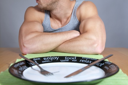 Muscular man sitting at the table with empty plateの写真素材