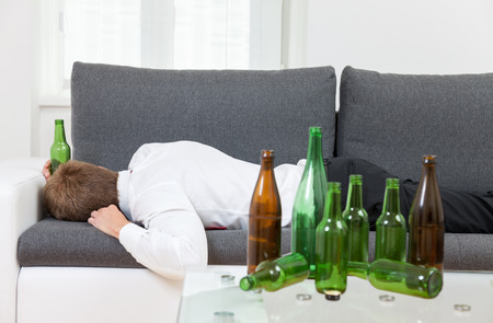 Depressed businessman drunk at home with empty bottles on tableの写真素材