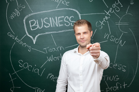 Young business man standing in front of a blackboard with a business planの写真素材