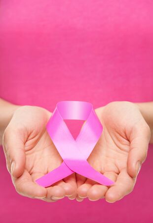 Woman holding a pink cancer awareness ribbon in her handsの写真素材