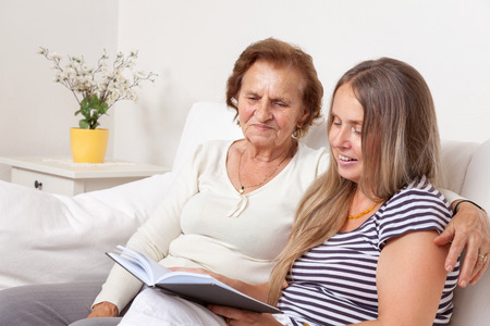 Carer spending time with an elderly woman by reading a bookの写真素材
