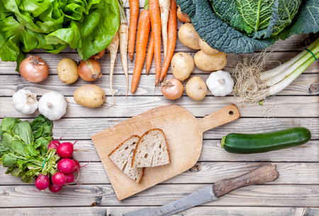 Freshly cut bread on chopping board with organic vegetables on wooden backgroundの写真素材