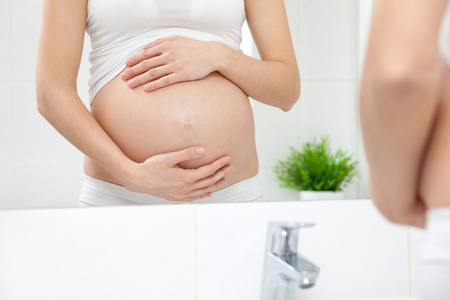 Pregnant woman in looking into bathroom mirrorの写真素材