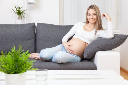 Beautiful pregnant woman relaxing at home on a sofaの写真素材