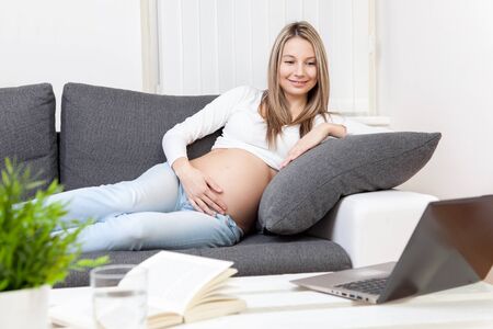 Beautiful pregnant woman relaxing at home on a sofaの写真素材