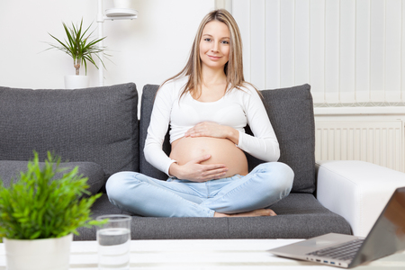 Beautiful pregnant woman relaxing at home on a sofaの写真素材