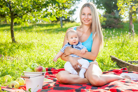 Beautiful mother with her baby sitting outdoors on a blanketの写真素材