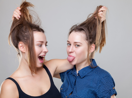 Studio portait of young and happy twin sisters fightingの写真素材