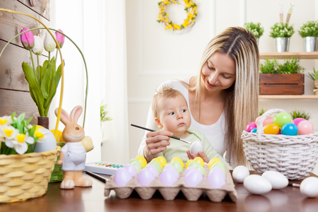 Easter concept. Happy mother and her cute child getting ready for Easter by painting the eggsの写真素材
