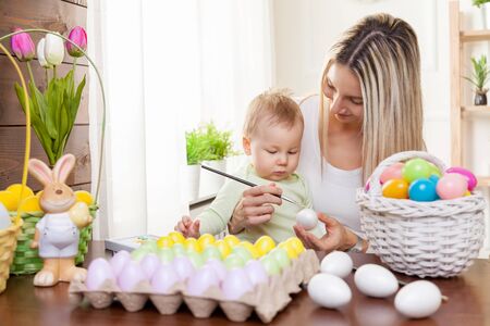 Easter concept. Happy mother and her cute child getting ready for Easter by painting the eggsの写真素材