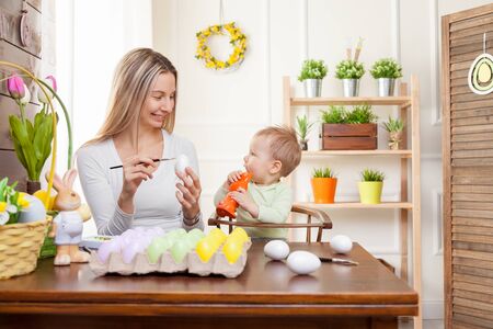 Easter concept. Happy mother and her cute child getting ready for Easter by painting the eggsの写真素材