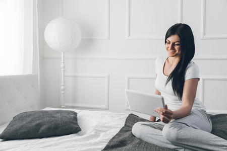 Beautiful young woman relaxing on the bed and using her tabletの写真素材