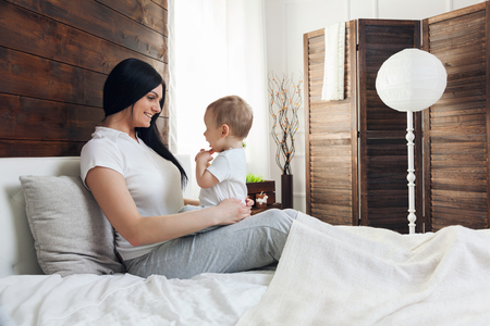 Happy mother with her cute little child on the bed having a good timeの写真素材