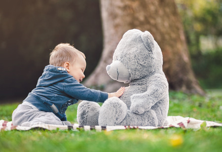 Best of friends. Sweet little toddler playing outdoors with his teddy bearの写真素材